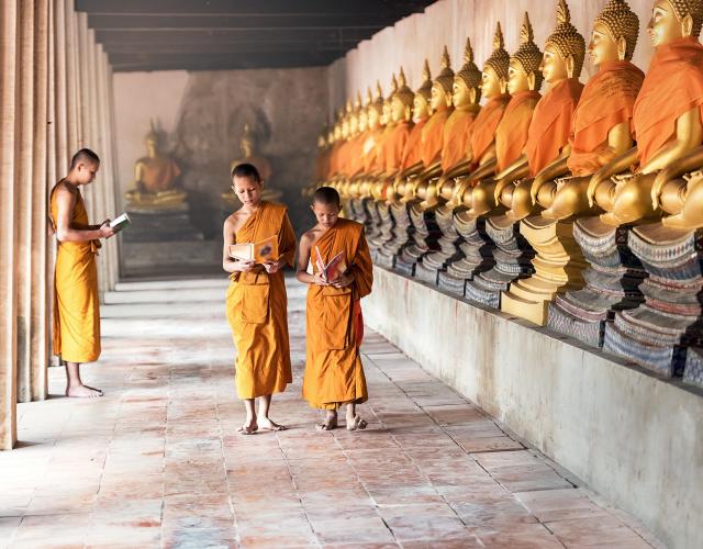 Two buddhist monks walking in temple, while one is standing and reading on left side